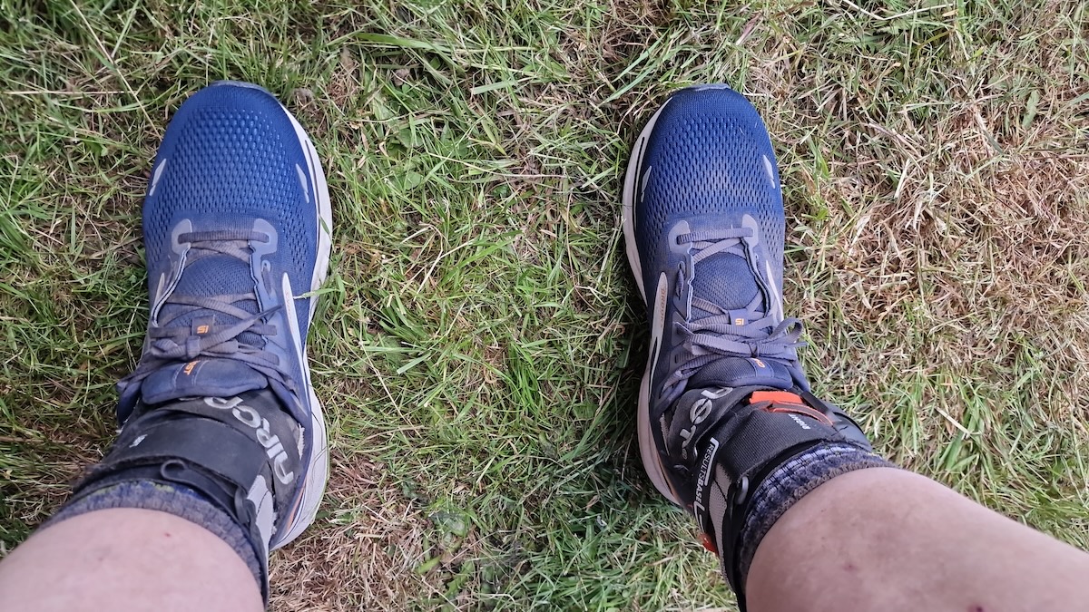 Photo looking down at a pair of feet wearing dusty running shoes and Aircast A60 ankle braces.